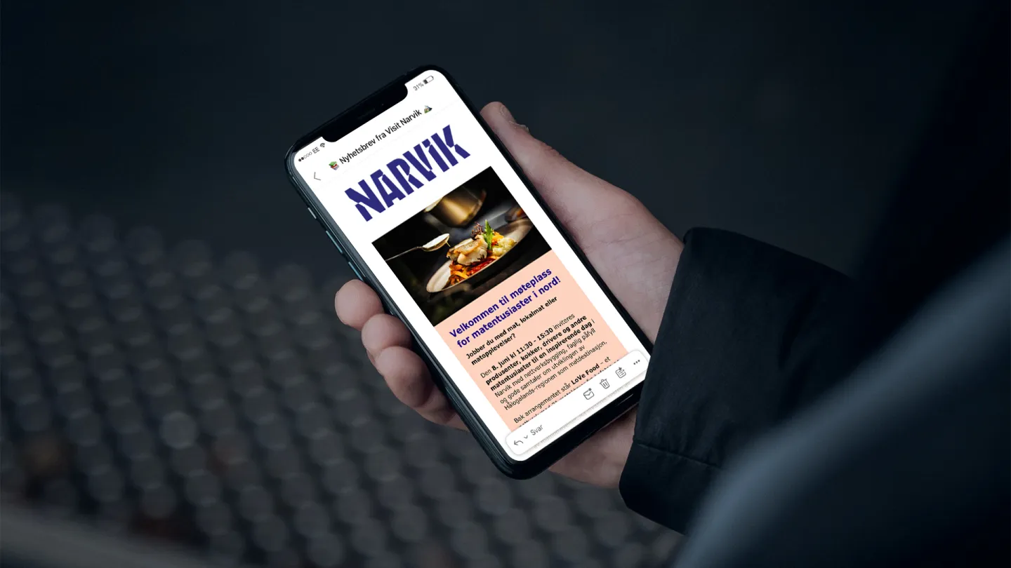 En hånd holder en smarttelefon som viser et nyhetsbrev fra Visit Narvik