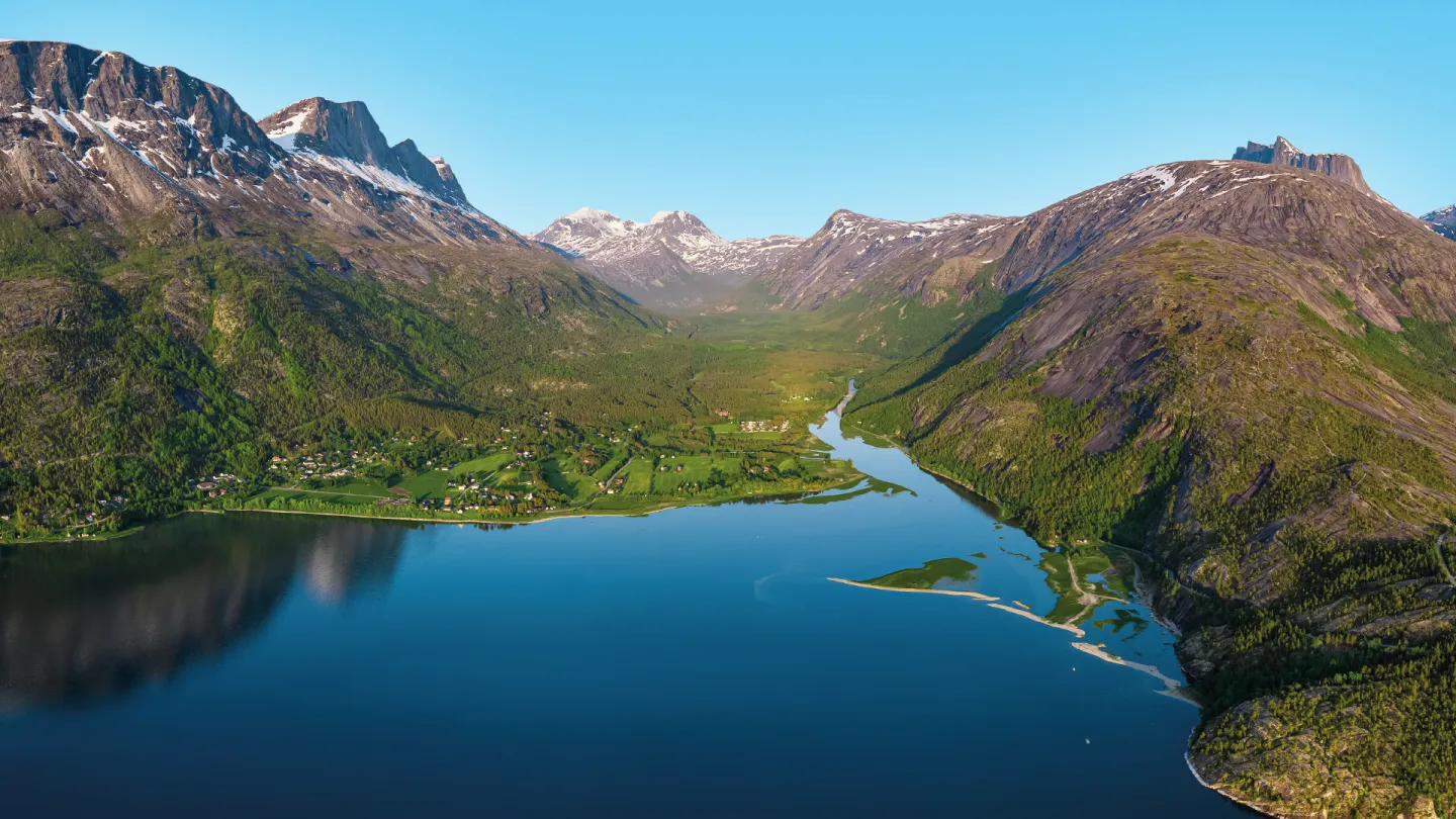 Panoramautsikt over Skjomen med grønne daler og høye fjell med snøflekker under klar blå himmel.