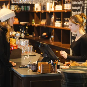 En kunde i lue og hettegenser står ved disken på Jernbanekaffen i Narvik mens en ansatt bak kassen tar imot bestilling i en kafé.