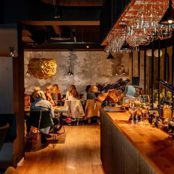 Innendørs atmosfære på Furu Gastropub i Narvik med lang bardisk, hengende vinglass og gjester som sitter ved bord i varmt lys.