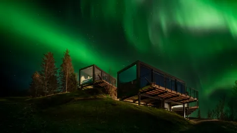 Nordlyset danser på himmelen over glasshyttene i Camp 291 i Narvikfjellet